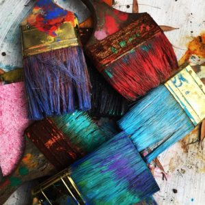 5 crossed paint brushes with a rainbow of color on them